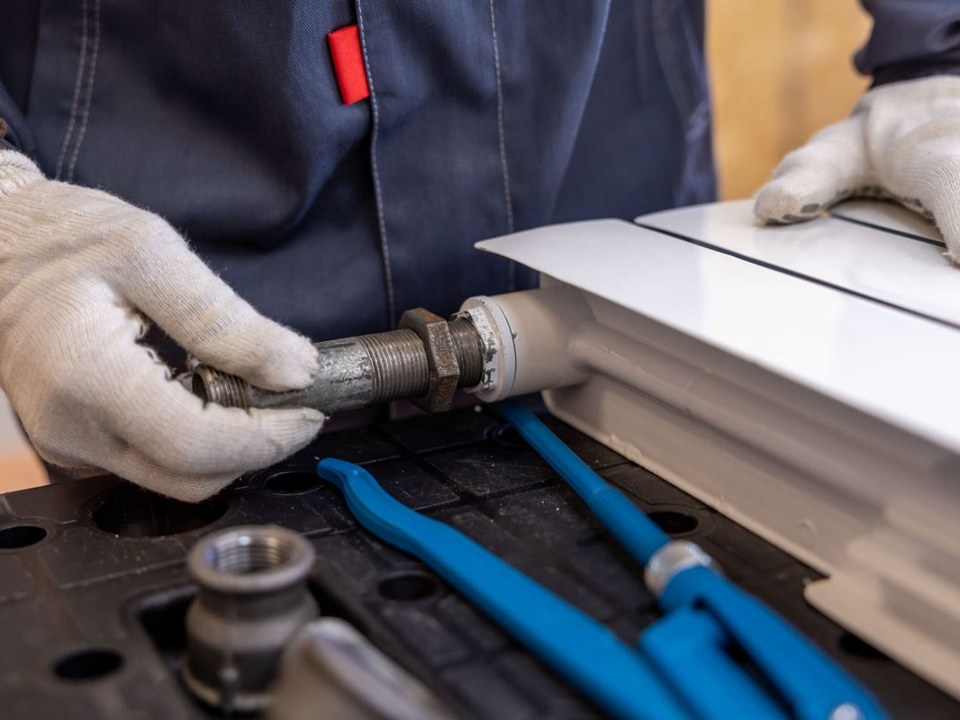 A plumber threading a pipe fitting, with blue pipe wrenches laid out beside the work