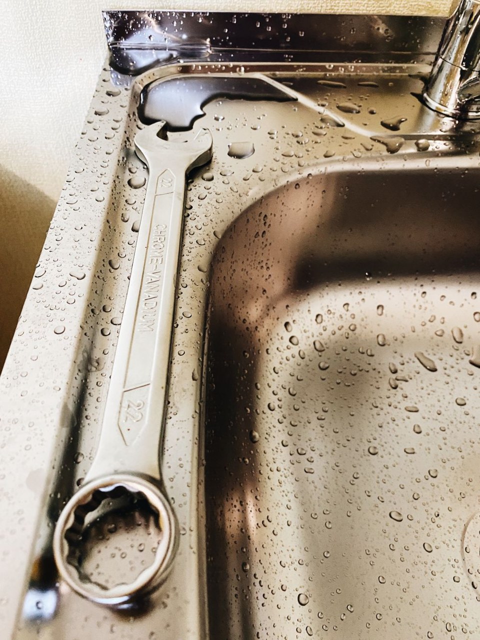 A combination wrench resting on the edge of a stainless steel sink during a repair
